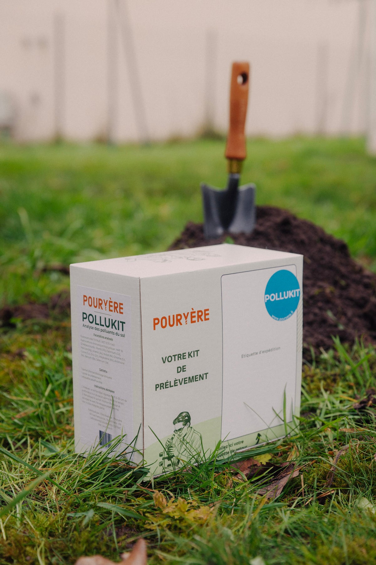 Kit de prélèvement Pouryère posé dans l'herbe devant un tas de terre fraîchement retournée avec une pelle plantée dedans